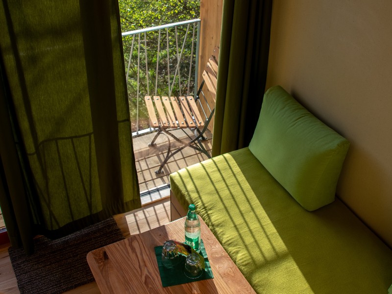 Ausblick vom Baumhaus-Hotel LandLust auf Balkon und Bäume. Die Wandheizung ist in der Rückwand des Sofas verschwunden